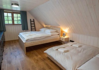 Manželská postel s výhledem do přírody, televizí a přistýlkou se nachází v jedné z ložnic Velkého apartmánu ubytování U Justina na břehu.